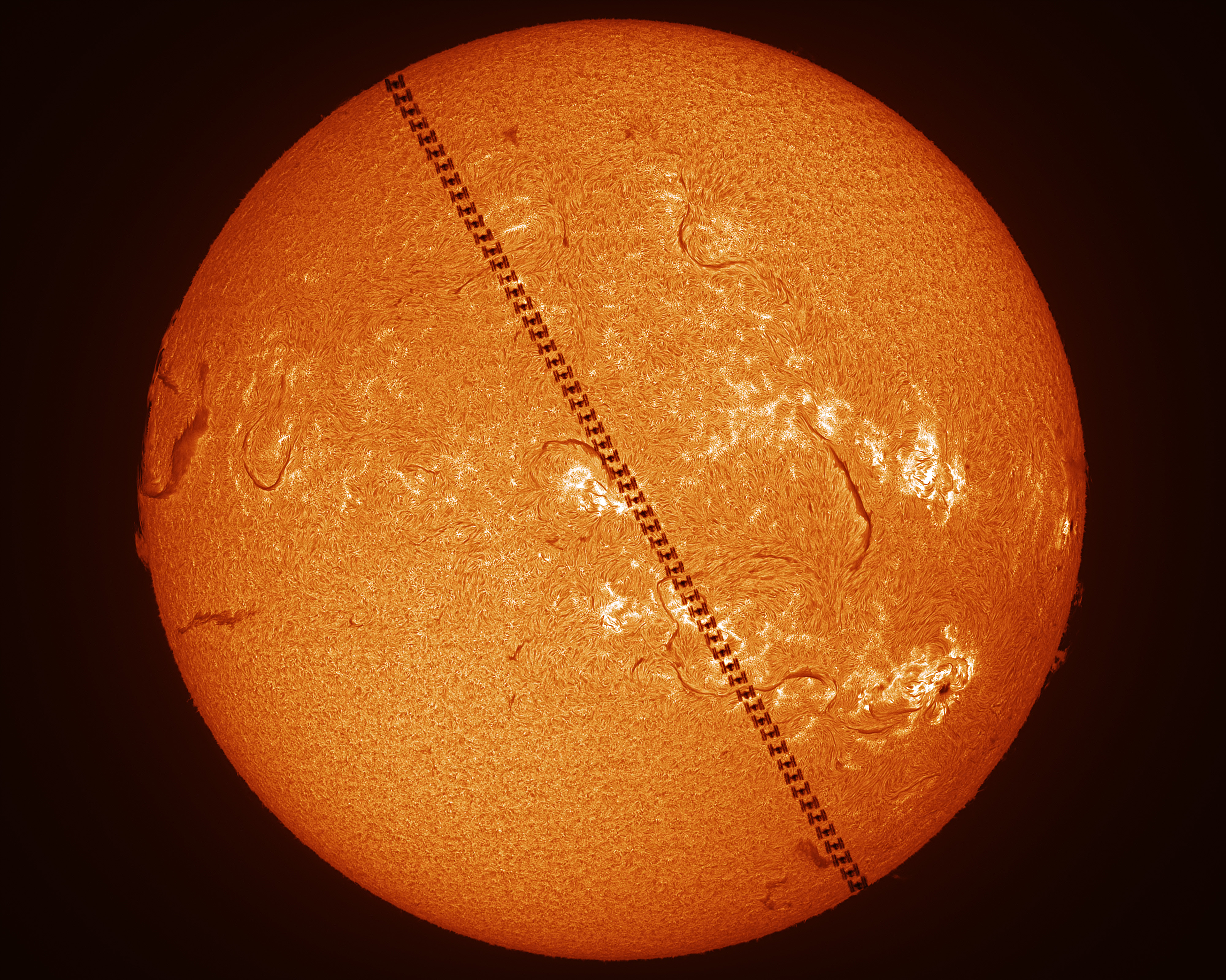 A close up of our Sun with a composite of the International Space Station seen moving diagonally across it
