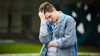 a young man holds his head in his hands looking confused