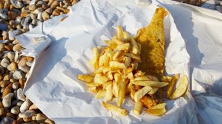 Fish and chips sitting in paper on a stoney beach