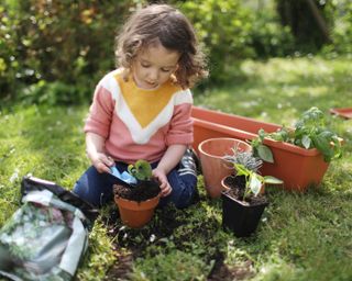 child potting up plants in a garden