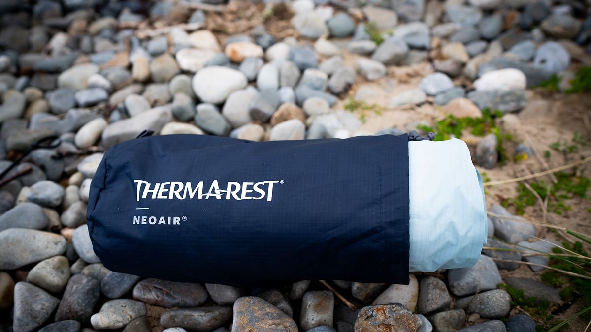 A Therm-a-Rest NeoAir XTherm NXT Sleeping Pad in its bag, on a stony beach.