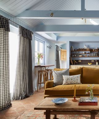 gingham curtains in a blue living room kitchen space with terracotta floor and a mustard sofa