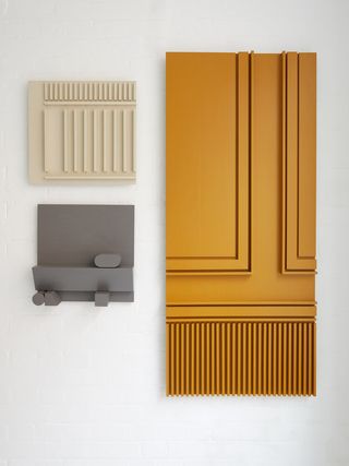 Contemporary craft wall sculptures (in grey, cream and orange) displayed on a white wall.