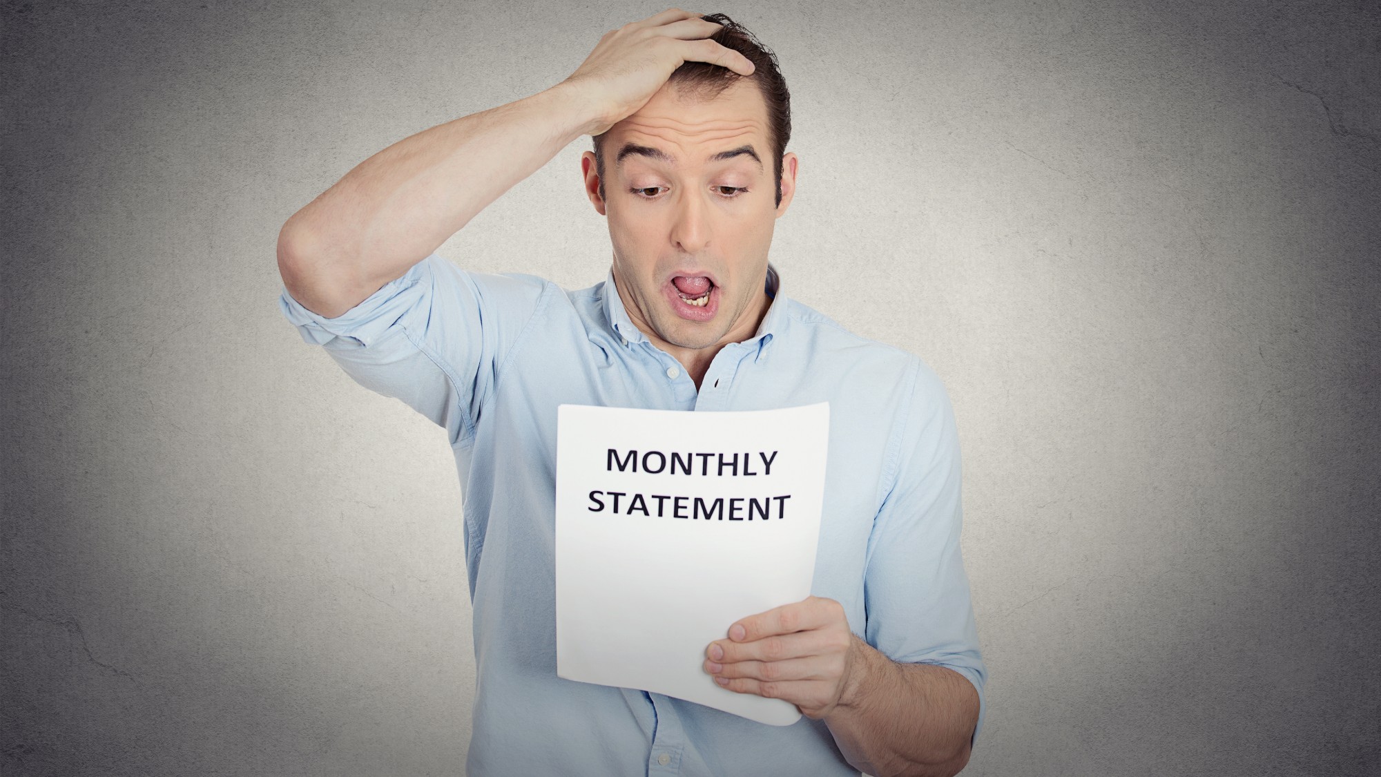Man holding his head and looking shocked as he reads a piece of paper marked "Monthly Statement"