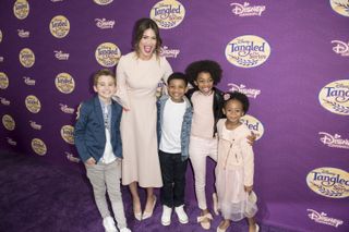 Mandy Moore stands with four children in front of a Tangled sign