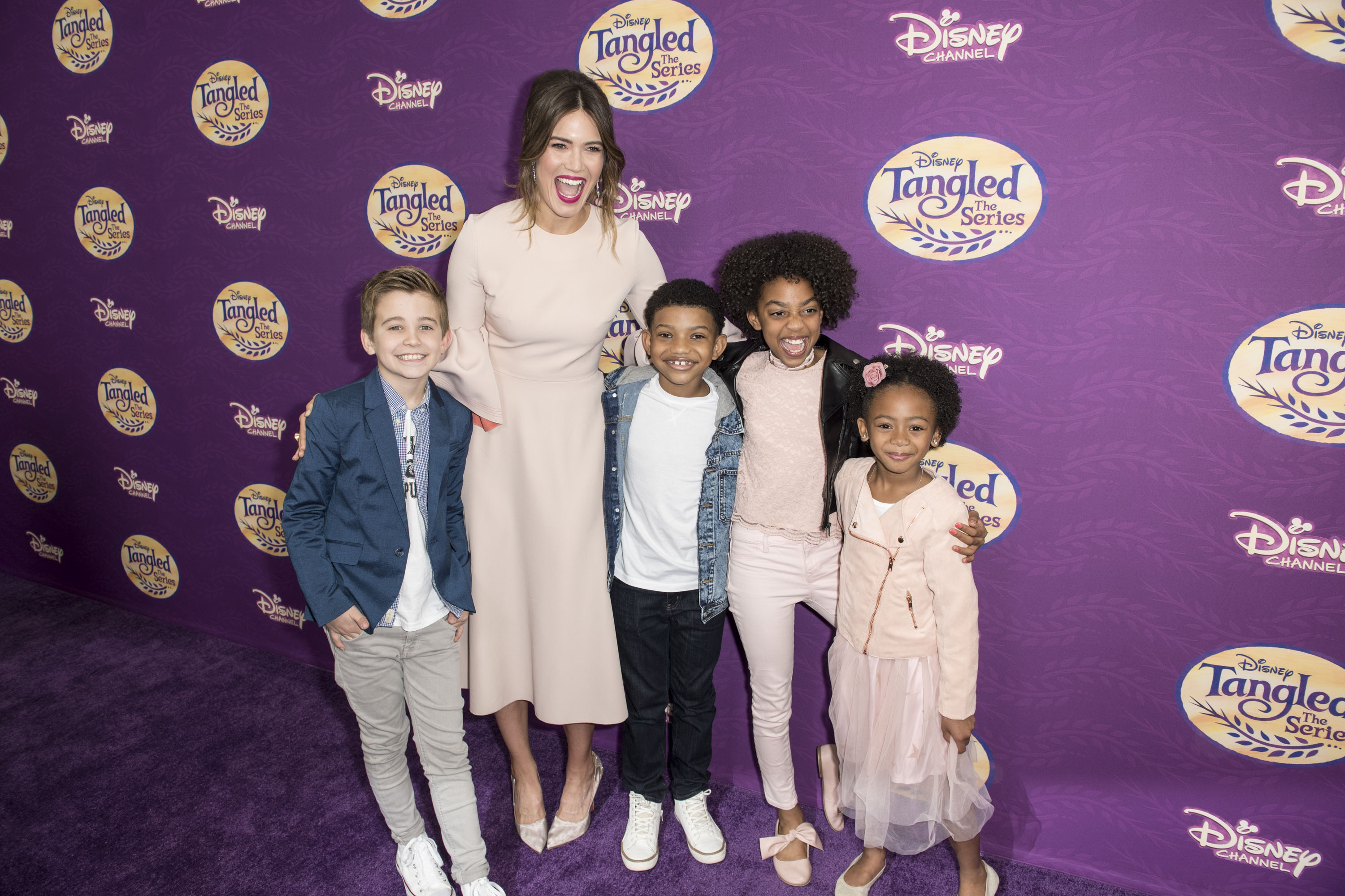 Mandy Moore stands with four children in front of a Tangled sign