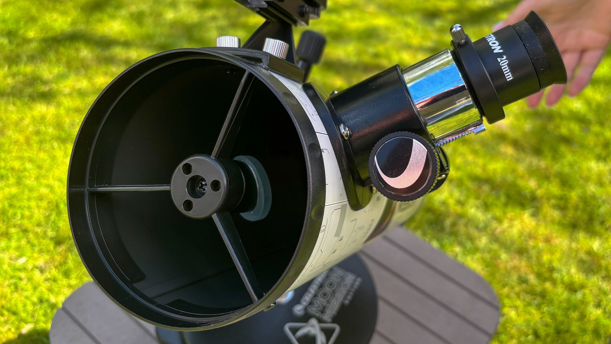 The apreture and eyepice on the Celestron Moon Mission 100mm Tabletop Dobsonian with grass in the background.