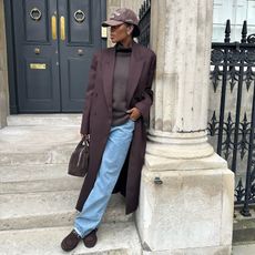 Fashion influencer @nlmarilyn in London wearing a chic winter look with a brown sweater, brown coat, and blue denim jeans, with brown accessories including a cap, suede loafers, and suede bowling bag.