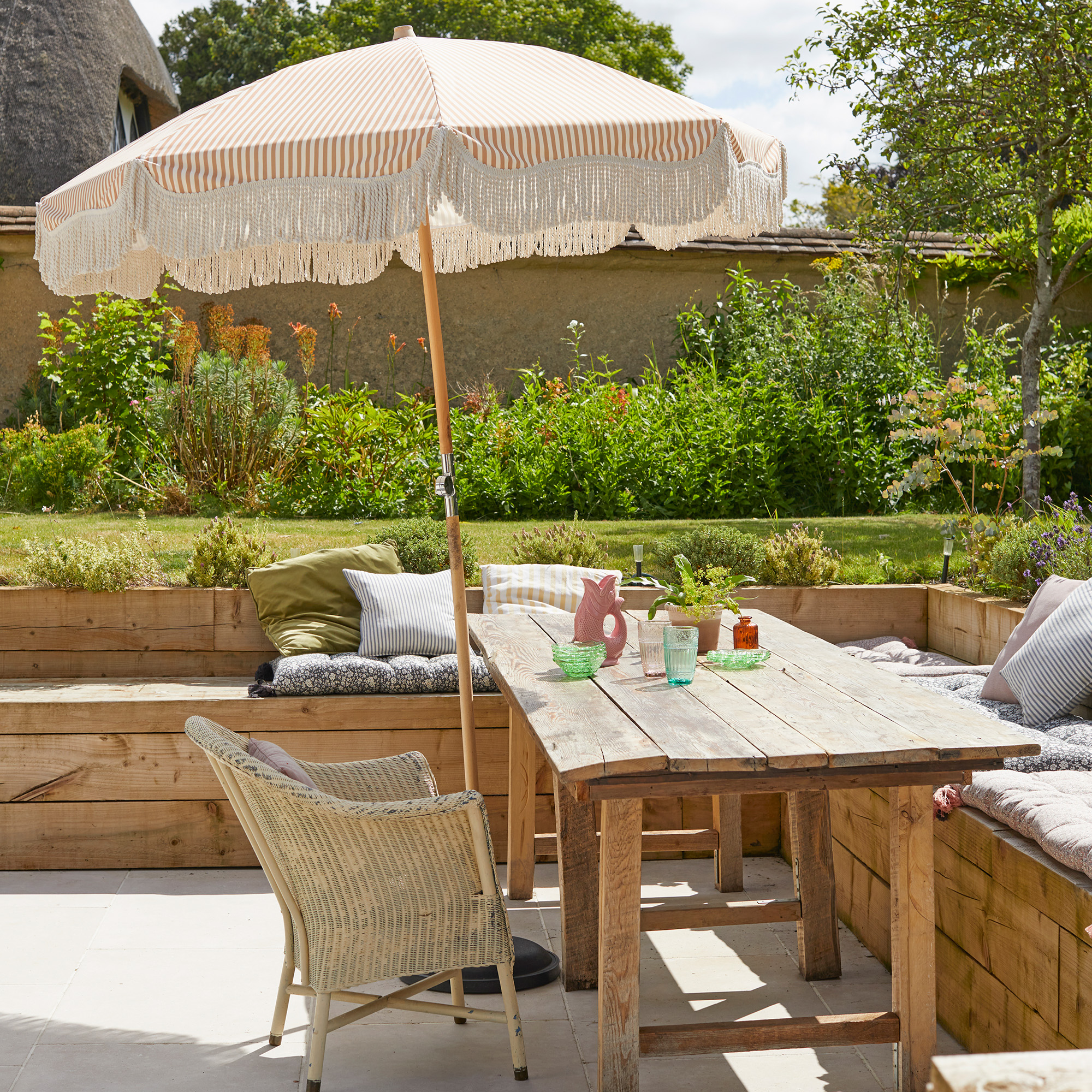outdoor dining area with wooden table and bench seating and a rattan armchair parasol is above