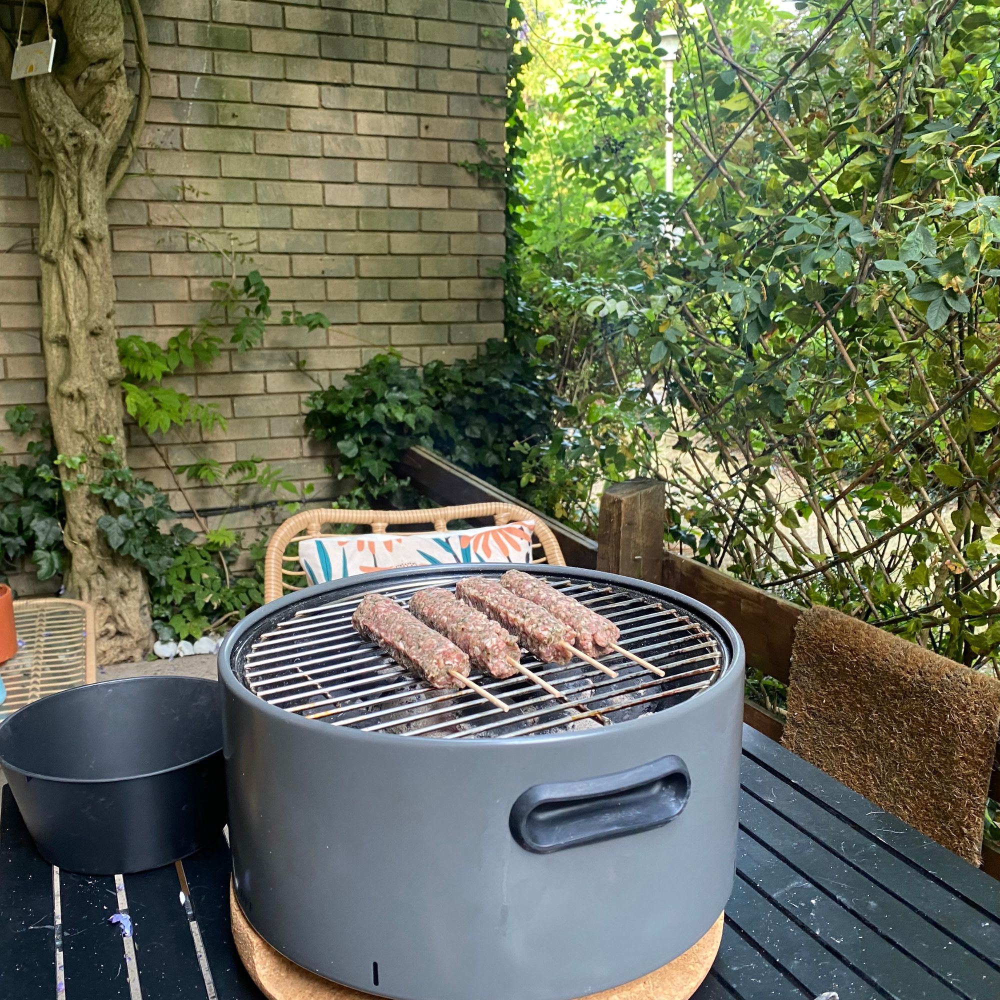 Portable BBQ on table in garden, cooking kebabs
