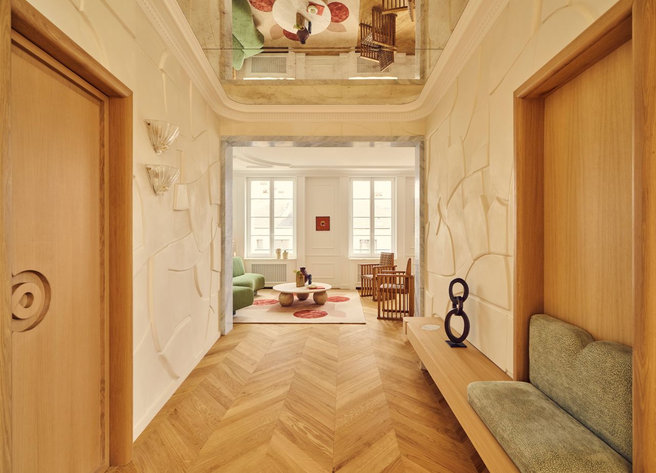 Batiik Studio-designed apartment entryway featuring an antiqued mirror ceiling, herringbone floors, and a sculptural bench with green cushions