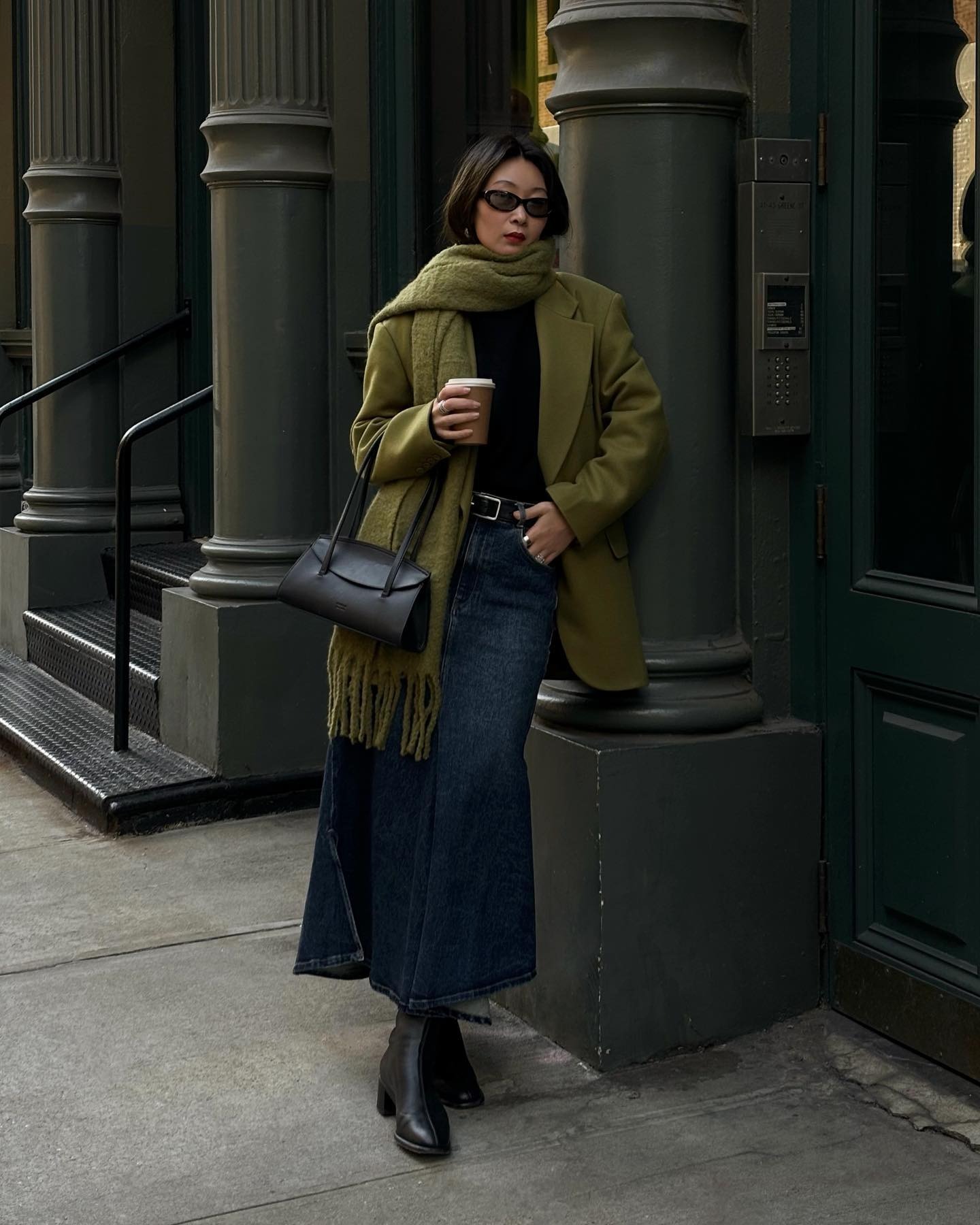 Caroline wears a green blazer, green scarf, maxi denim skirt, black boots and black bag