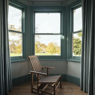 Wooden chair in reading nook with three large windows.