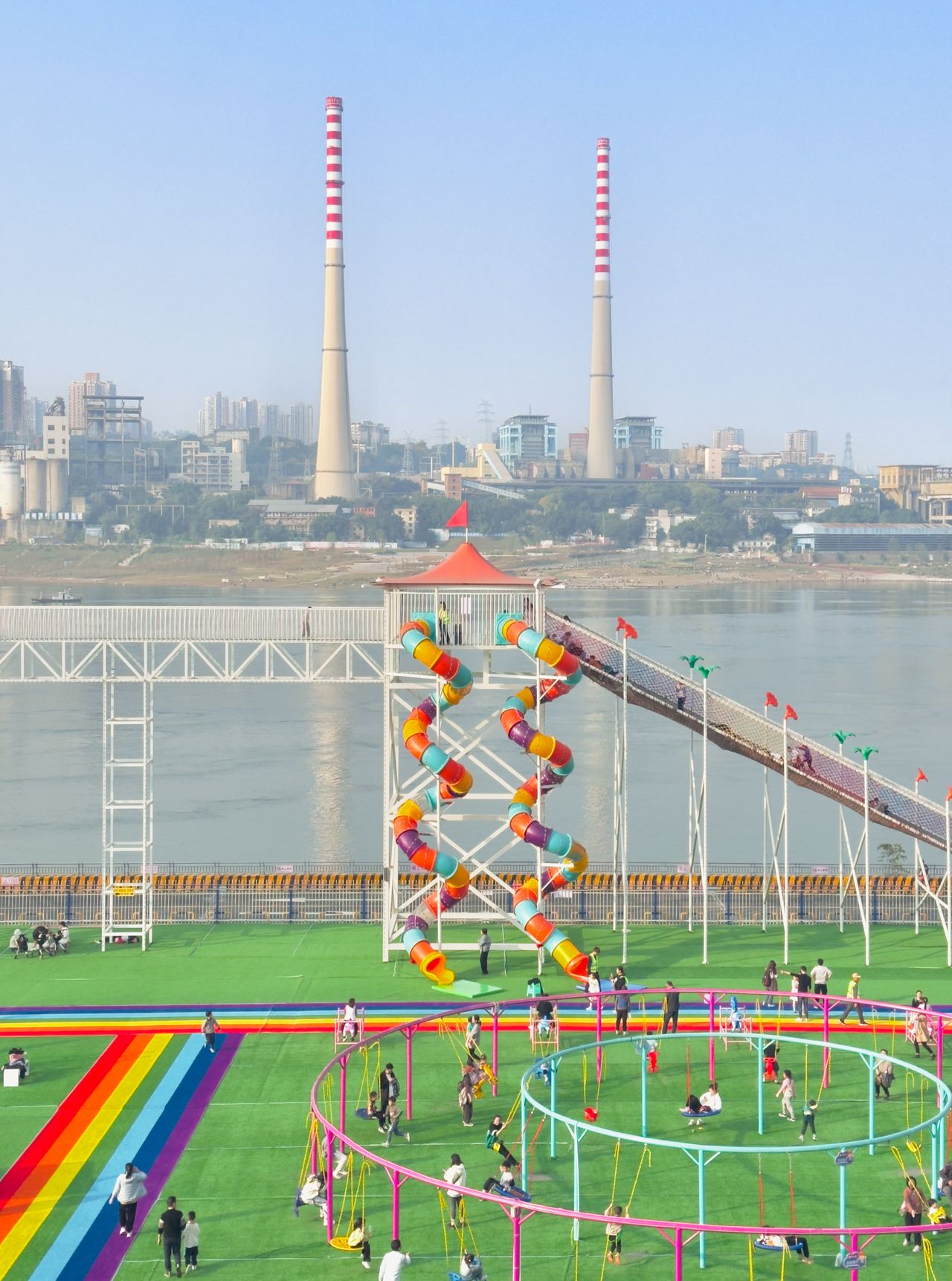A colorful playground in front of a river and industrial towers