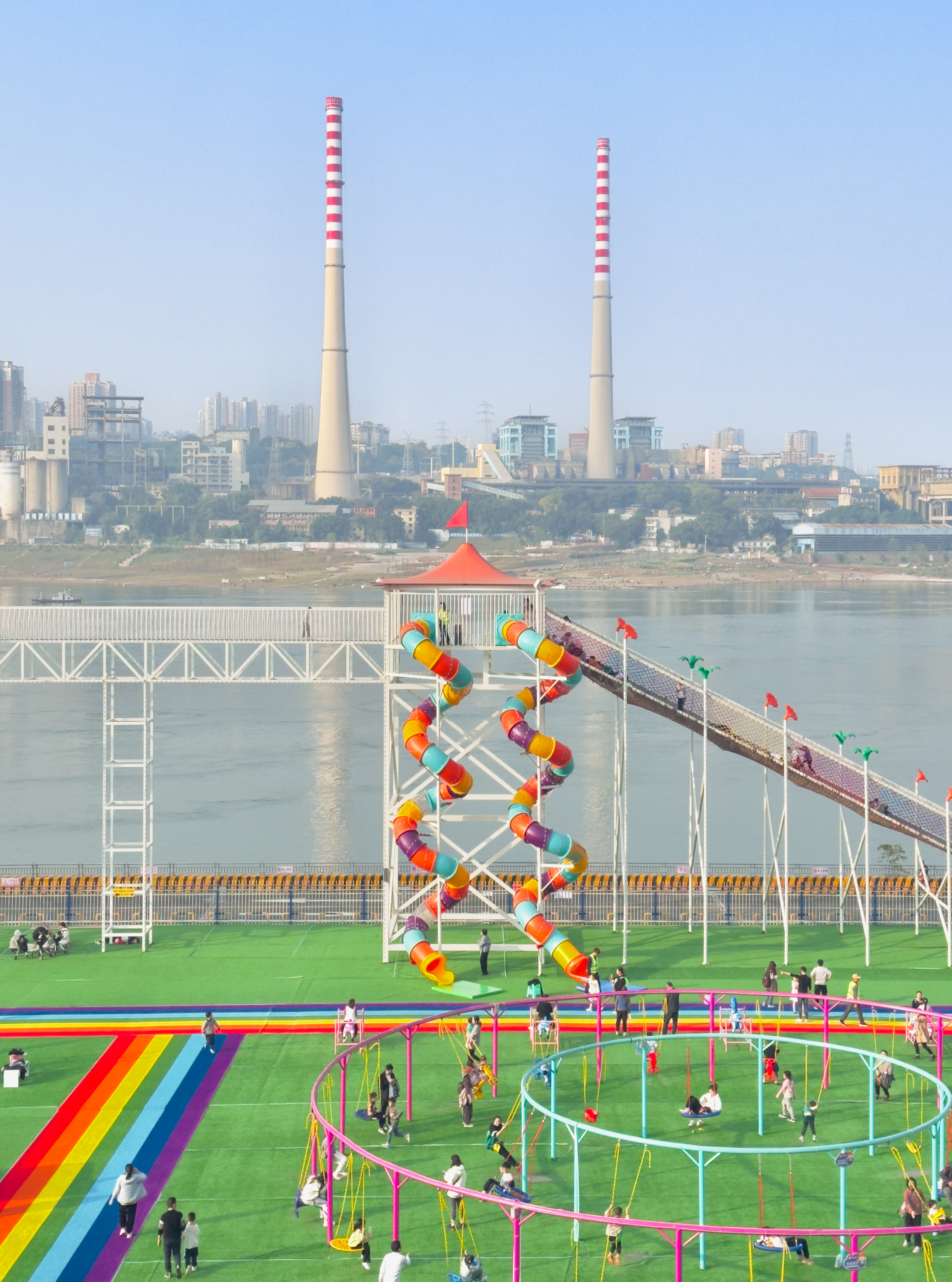 A colorful playground in front of a river and industrial towers