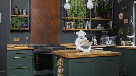 Green Shaker-style kitchen with wood worktops, copper splashback, pendant lights and black floorboards