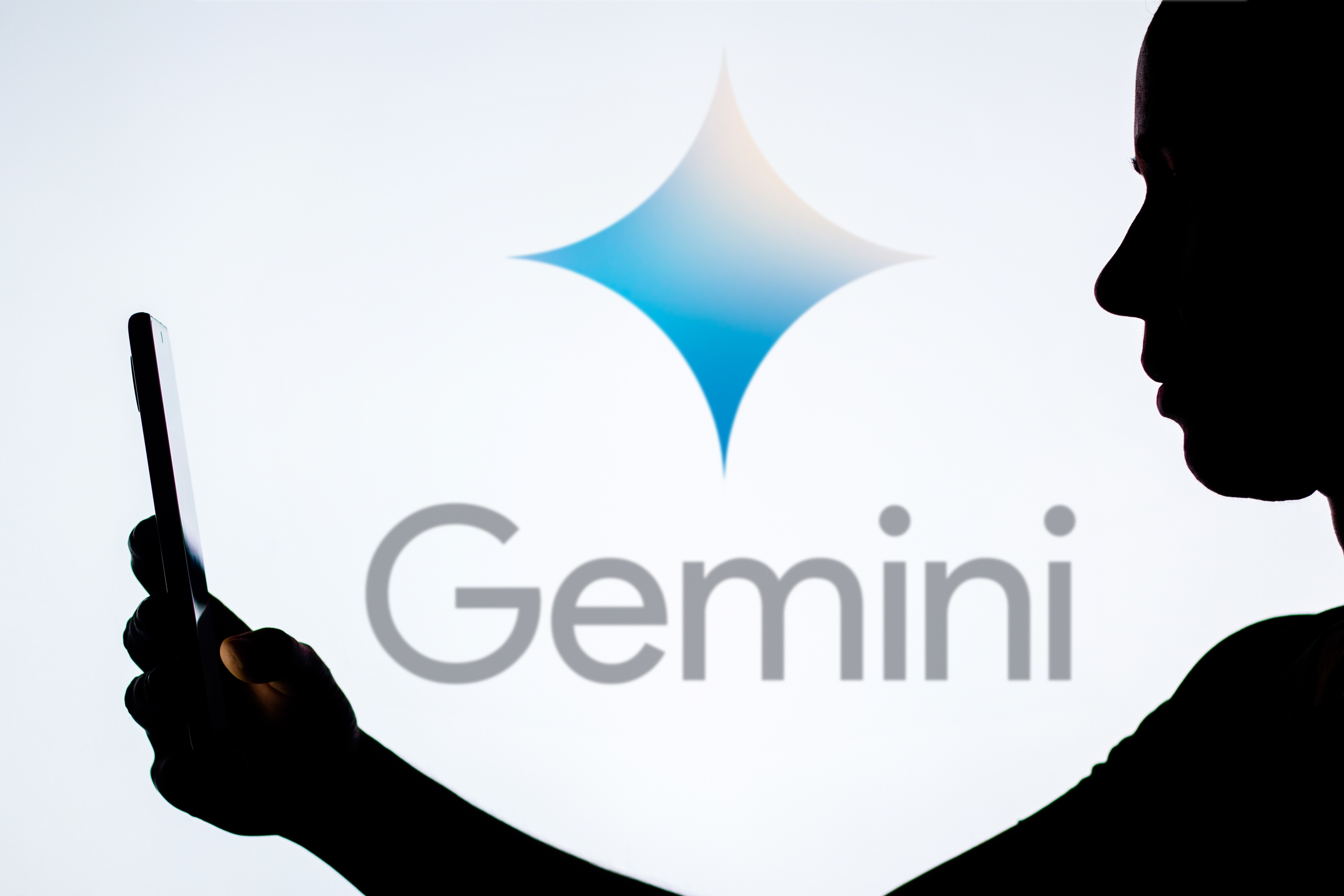 Logo Google Gemini dengan orang yang memegang telepon