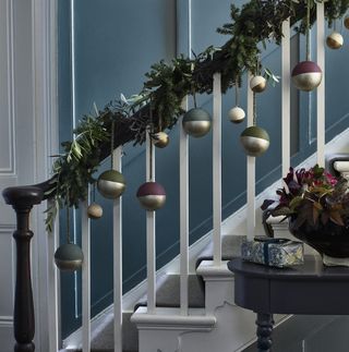 Black and white balustrade decorated with green garland and baubles hanging from it next to hallway table with gift and plant on top