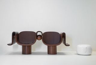 View of the wooden 'Shiya' double seat and a white version of the ‘Loma’ stool by Mabeo for Fendi pictured against a light grey background