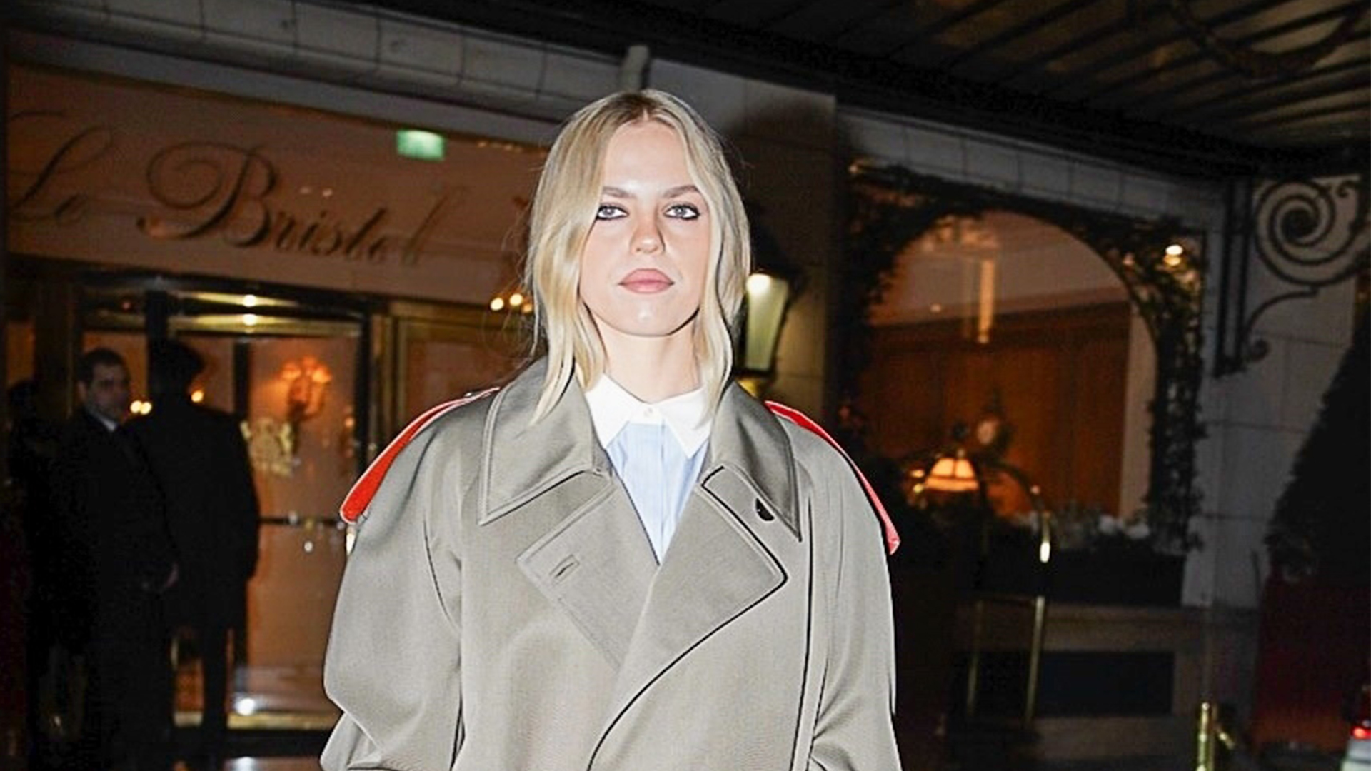 Renee Rapp wearing a Tory Burch trench, striped button-down shirt, and red heels