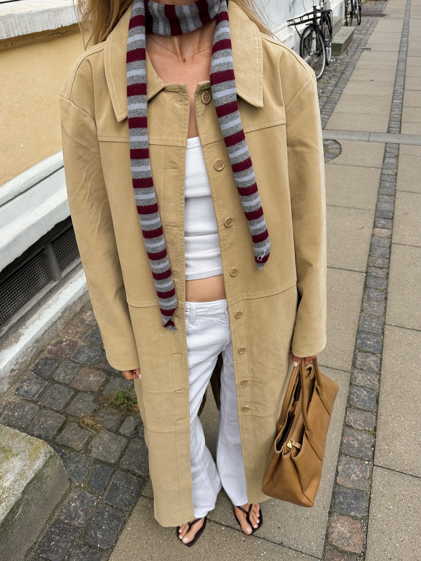 An image of @chloekathbutler wearing a butter yellow trench coat with white jeans and a striped scarf.