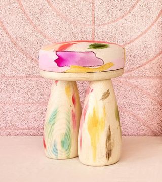 A hand-painted stool in wood against a pink textured wall.