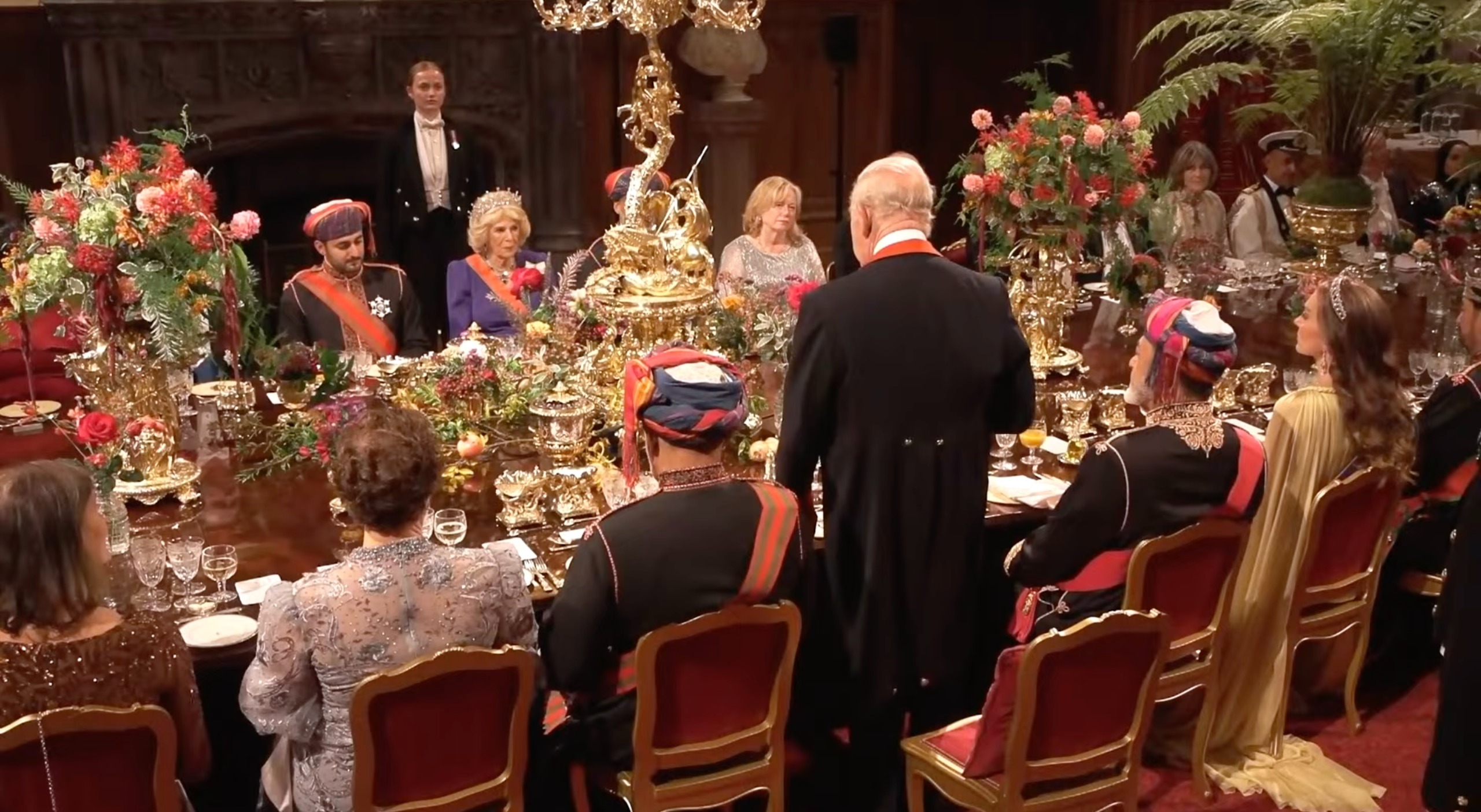 Princess Kate sitting at a banquet table next to King Charles, standing giving a speech