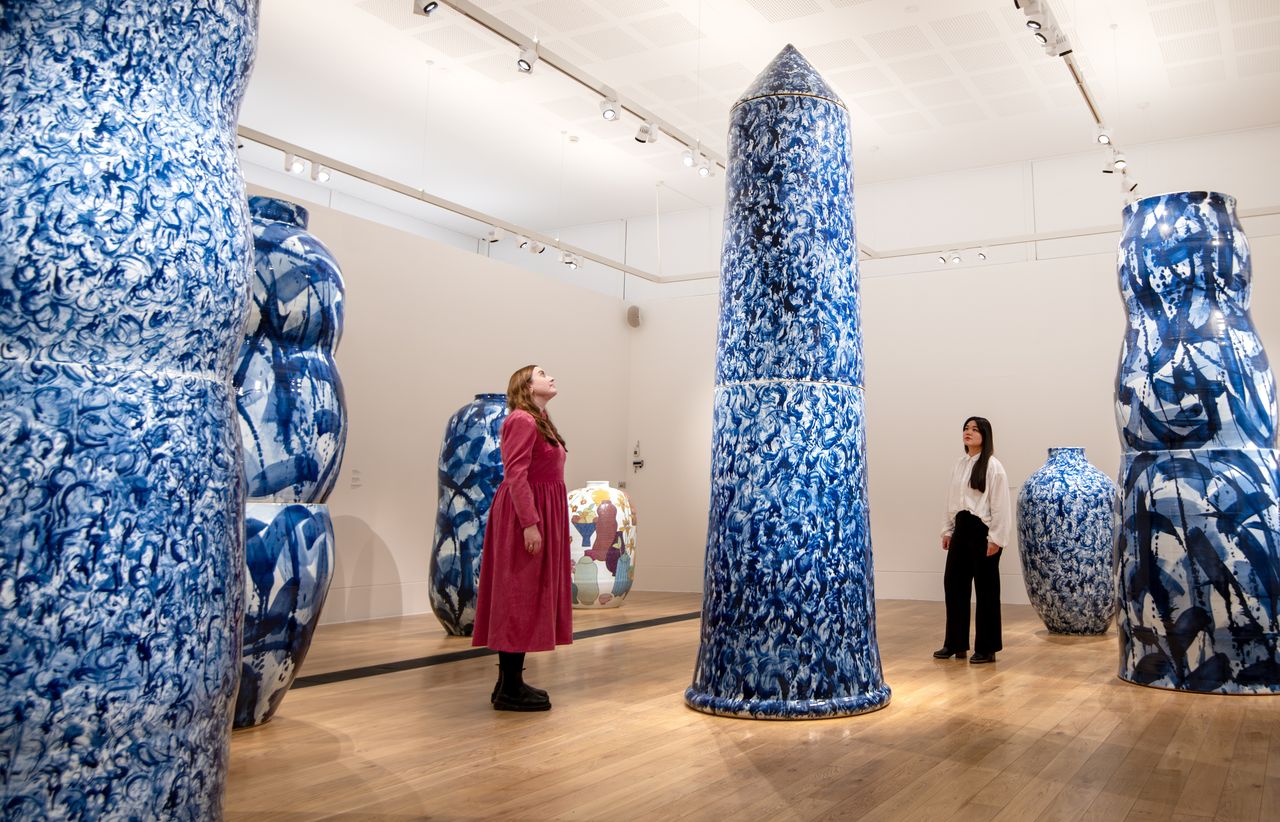 A series of gigantic china-style vases is on display in a warmly lit gallery, including some blue and white pieces and some more widely colored ones.