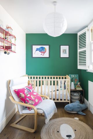 Nursery with green feature wall, wood floor, jute bear rug, wooden cot and armchair and whale toy