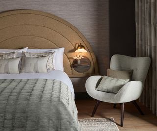 bedroom with arched sand coloured headboard, pale green chair and bed with white bedding and pale green throws and cushions