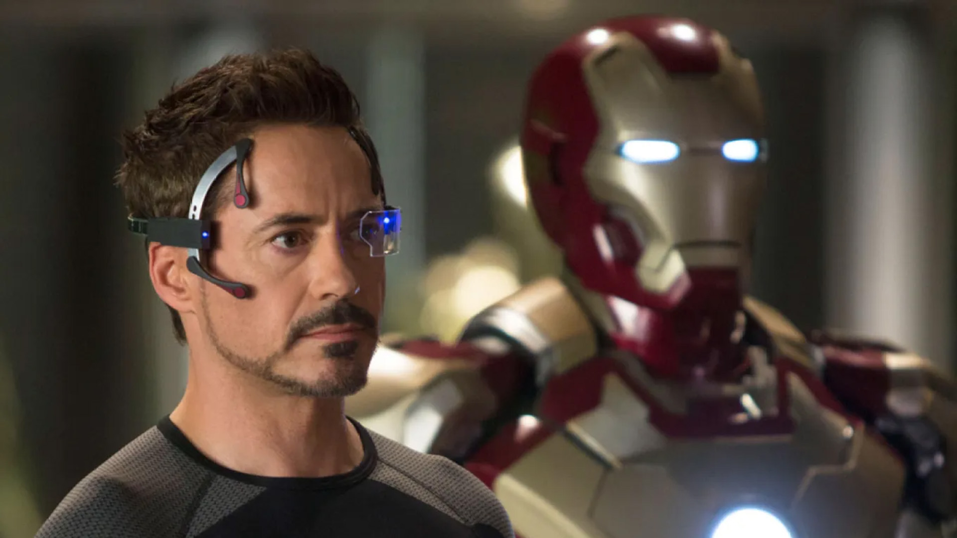 Robert Downey Jr. as Tony Stark next to an Iron Man suit in Iron Man 3.