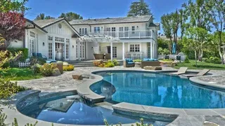 Exterior of a large white house with a pool and patio in the foreground