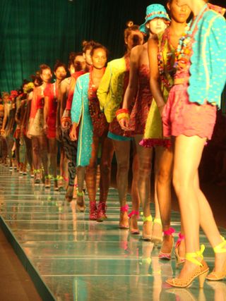 A long line of models on the runway, all wearing brightly-coloured clothing and accessories