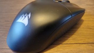 A black Corsair Katar Elite Wireless gaming mouse on a brown wooden table