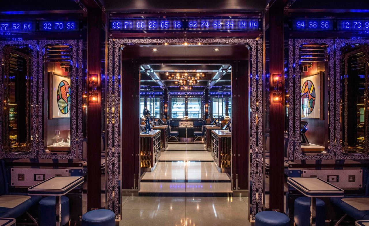 Hallway at Bob Bob Cité restaurant which has white and blue striped tables, round blue chairs, wall mirrors and a strip of glowing blue numbers running below the ceiling.