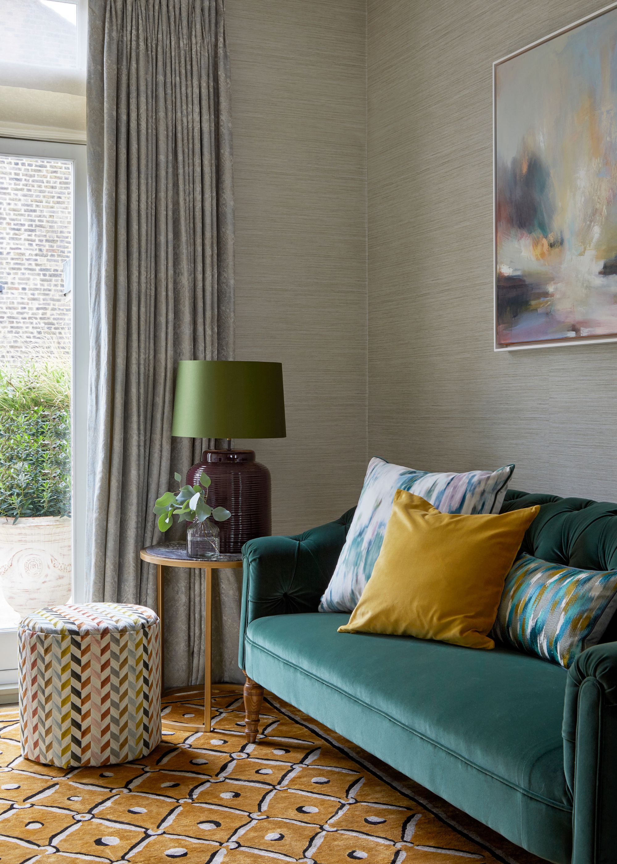 A living room with a teal sofa, neutral walls, an ochre rug and gray curtains.