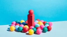 A group of multicoloured spheres around a single red sphere on a pedestal