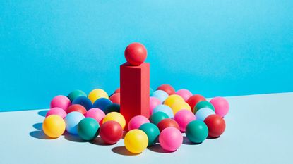 A group of multicoloured spheres around a single red sphere on a pedestal