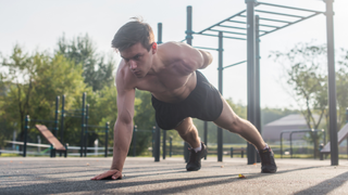 Man performing one-arm push-up outdoors with right hand down and left arm behind back