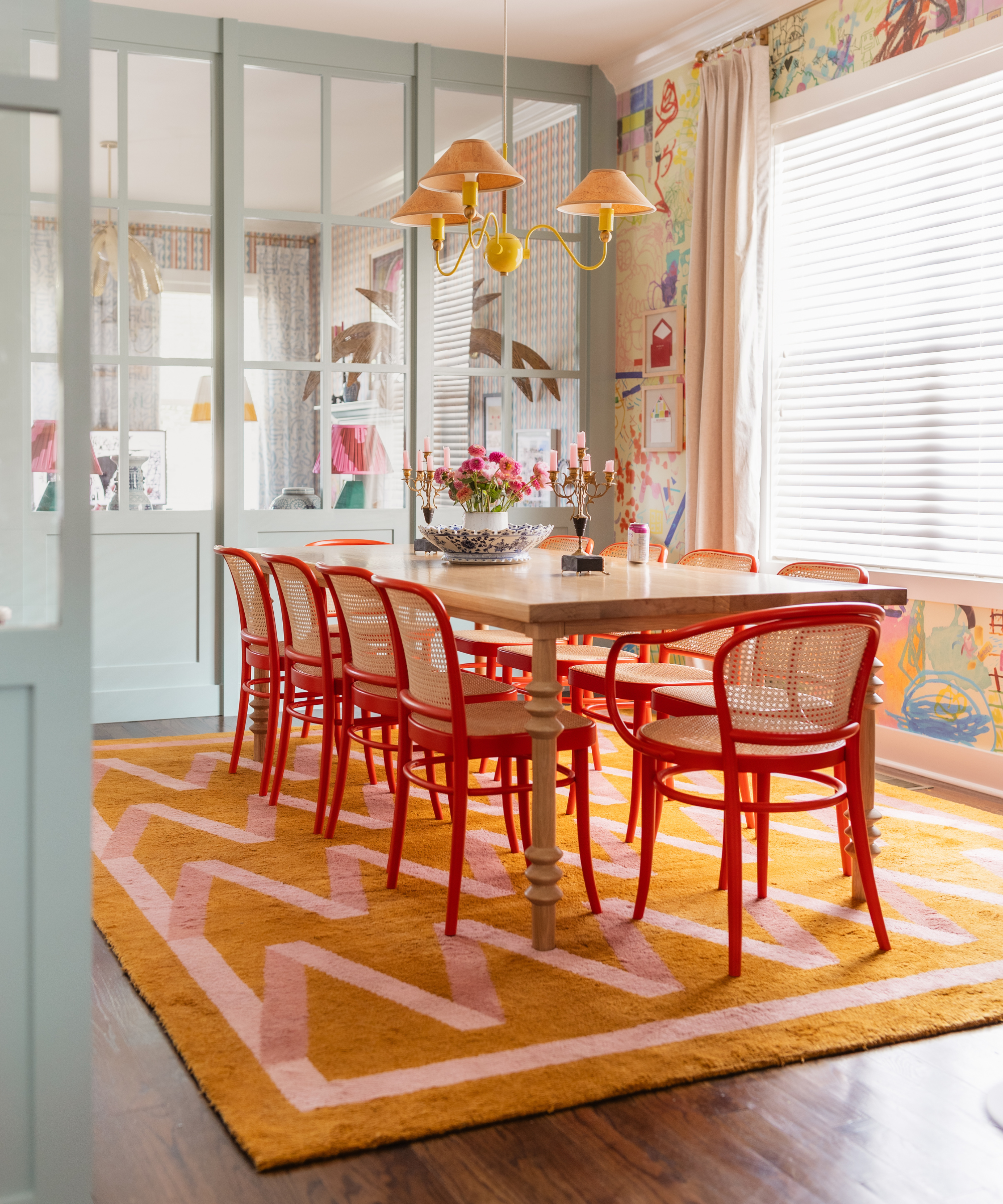 a dining room with a long dining table with red dining chairs and an orange and pink zig zag rug