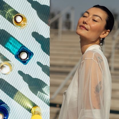 a woman with glowing skin in a white sheer shirt next to a light blue table with colorful skincare bottles