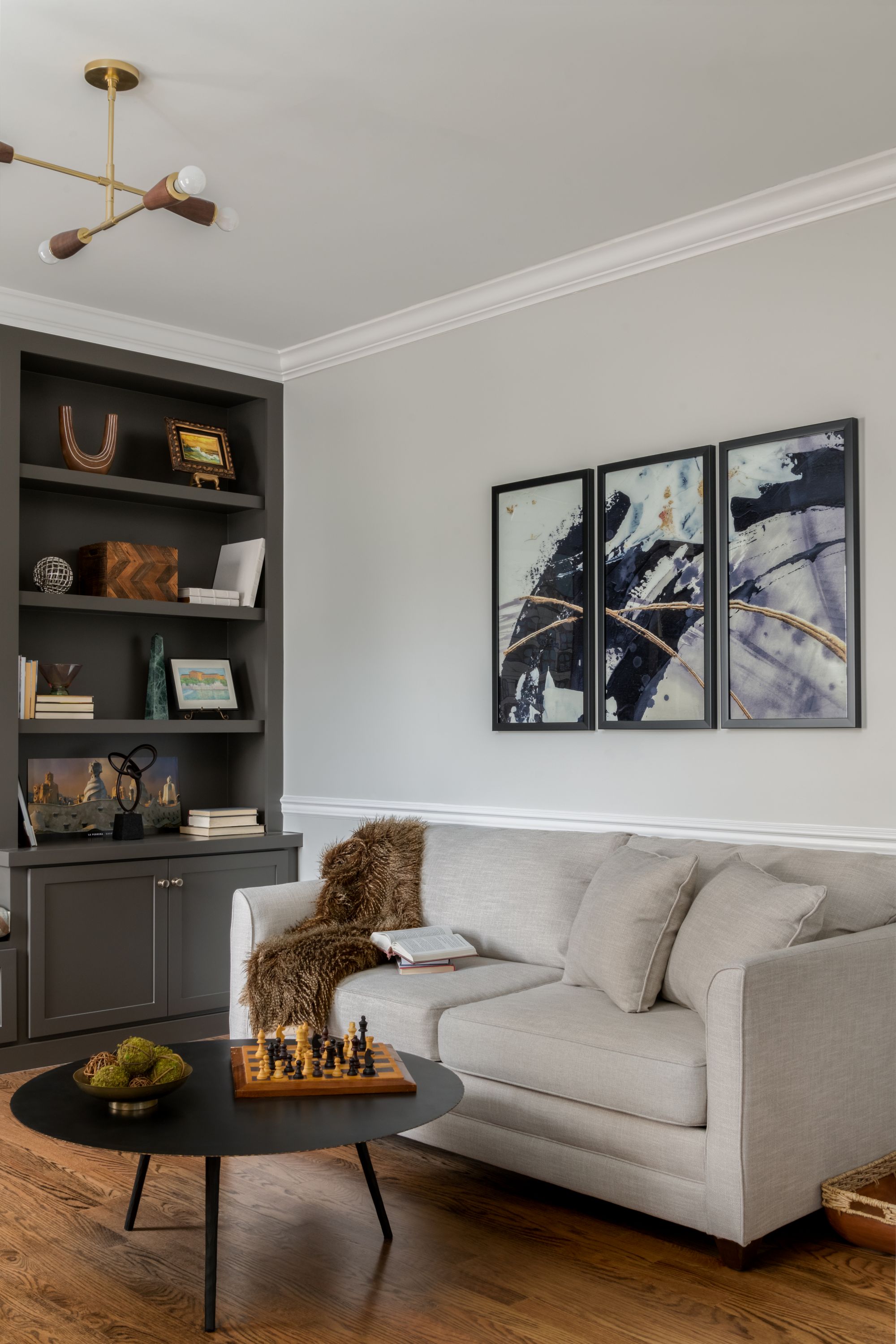 a small black coffee table, a cream colored couch, and three abstract images above the couch