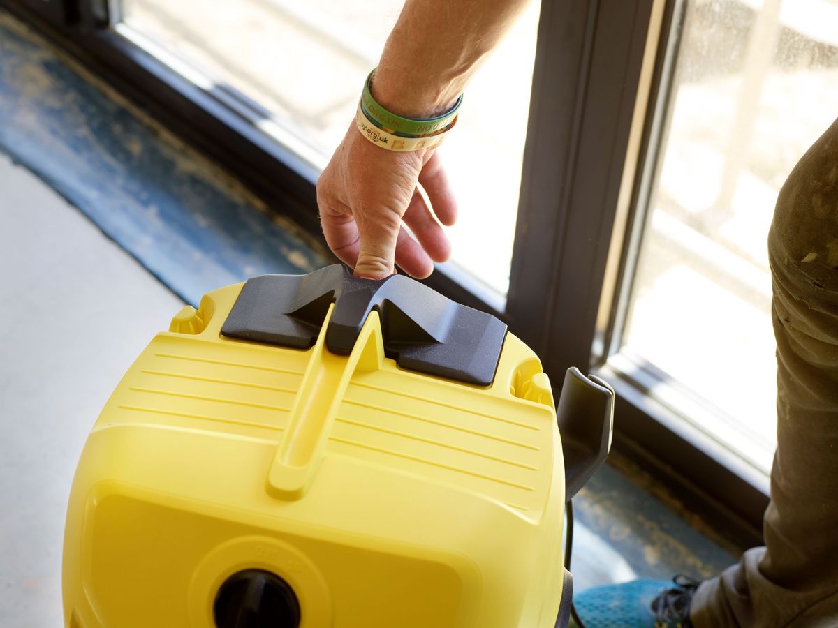A man pressing on the pop out filter button on a Karcher WD 4 vacuum cleaner