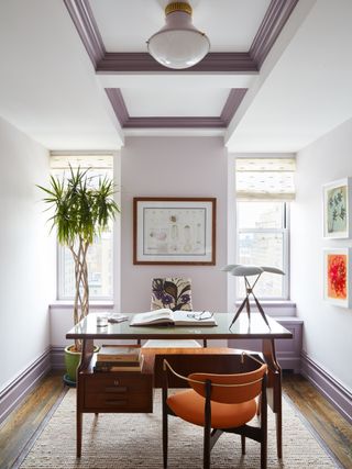 small home office with white and two tone lavender walls, dark lavender woodwork, retro desk and chair, plant, retro desk lamp, artwork, rug