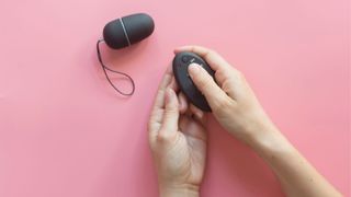 Remote control kegel ball with woman's hands holding controller on pink background