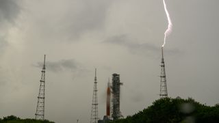 lightning strikes a lightning tower to the right of a big red rocket