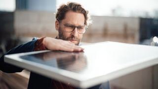 man with beard and glasses stood holding and looking at solar panel