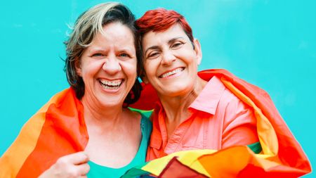 Happy senior lesbian couple wearing Lgbtq rainbow flag