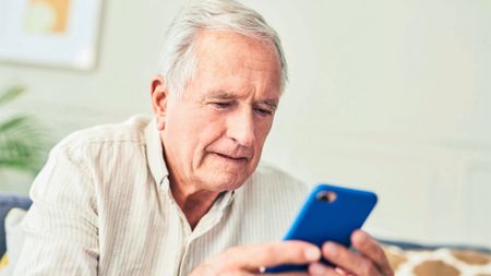 Close up of senior man using his cellphone while sitting at home