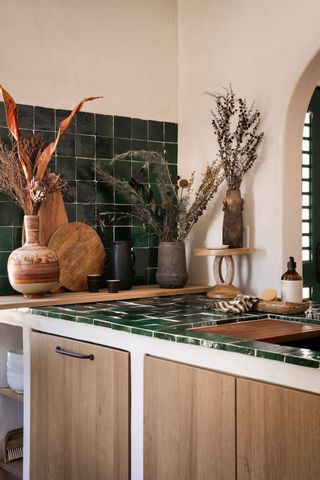 A small kitchen with dark green zellige tiles on the counter